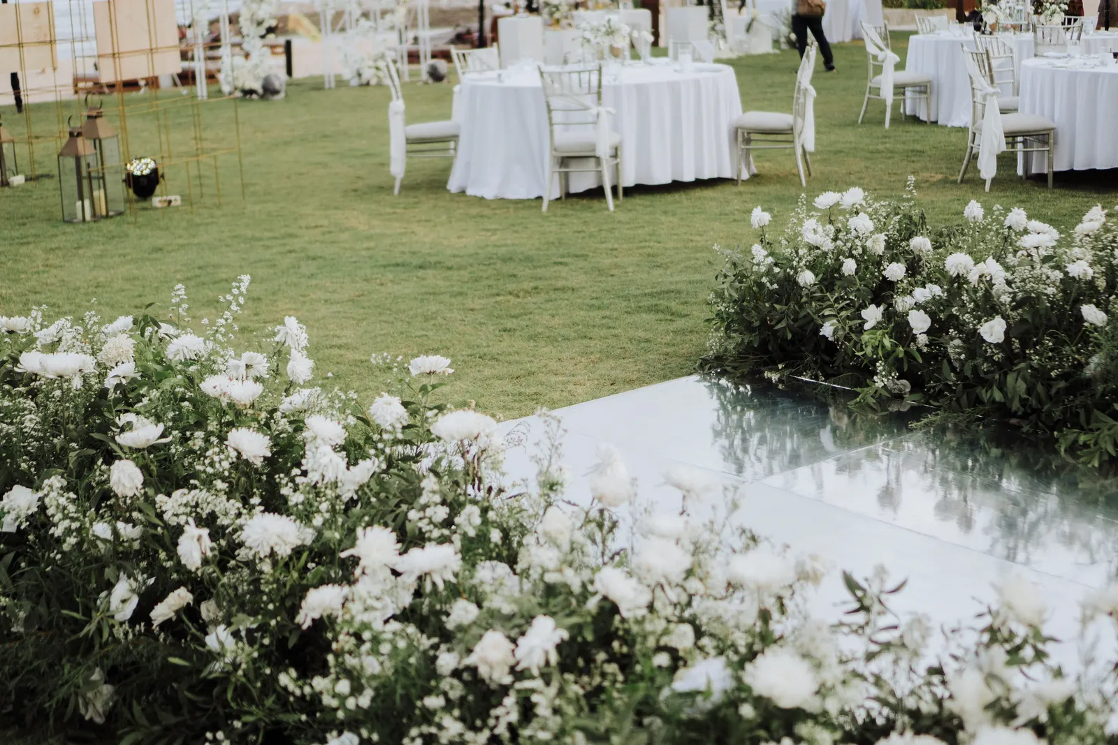 Mirror dance floor bordered with white florals, dining tables set on the lawn beyond
