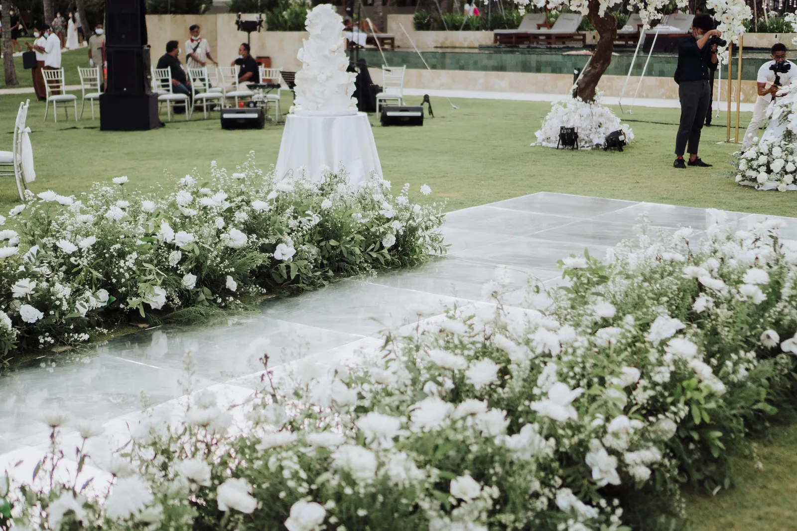 Mirror dance floor and cake table under blossom trees, guests in the distance
