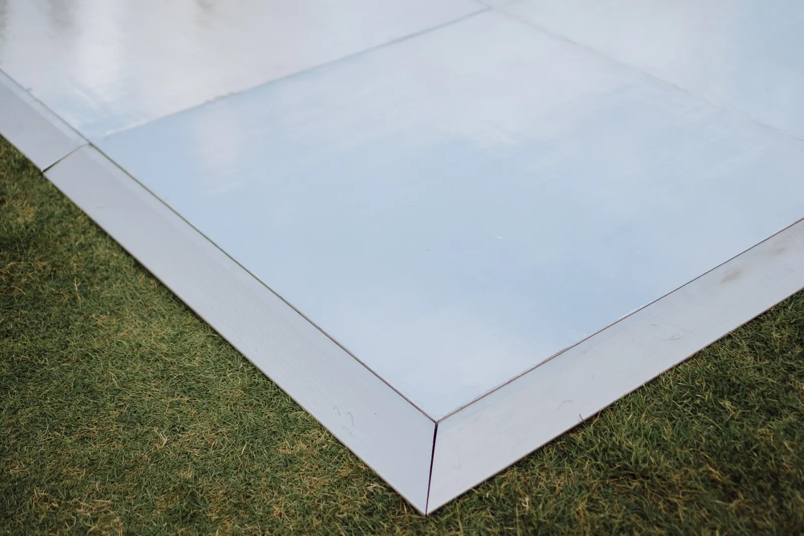 Corner of the mirror dance floor laid directly on the grass, showing the panel edge and finish