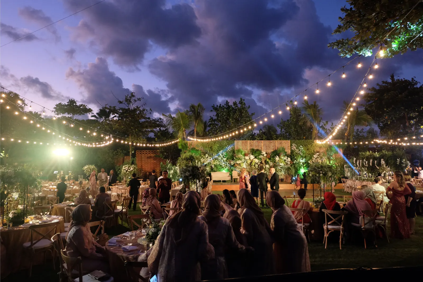 Guests seated at the long tables at dusk, festoon lights overhead
