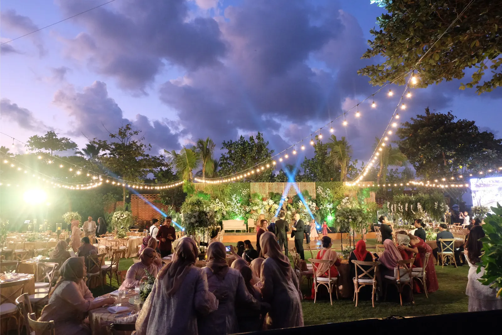The party at dusk, guests standing and talking under the lights