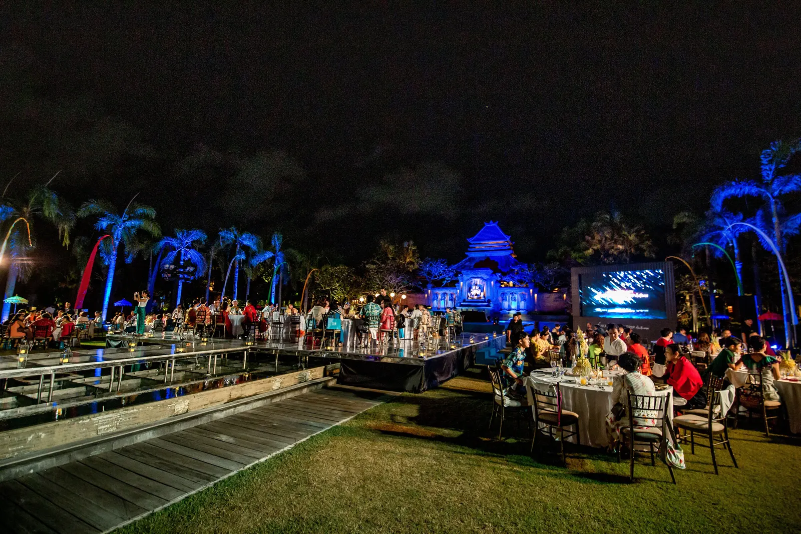 Guests around the acrylic floating stage at night, coloured lighting across the water